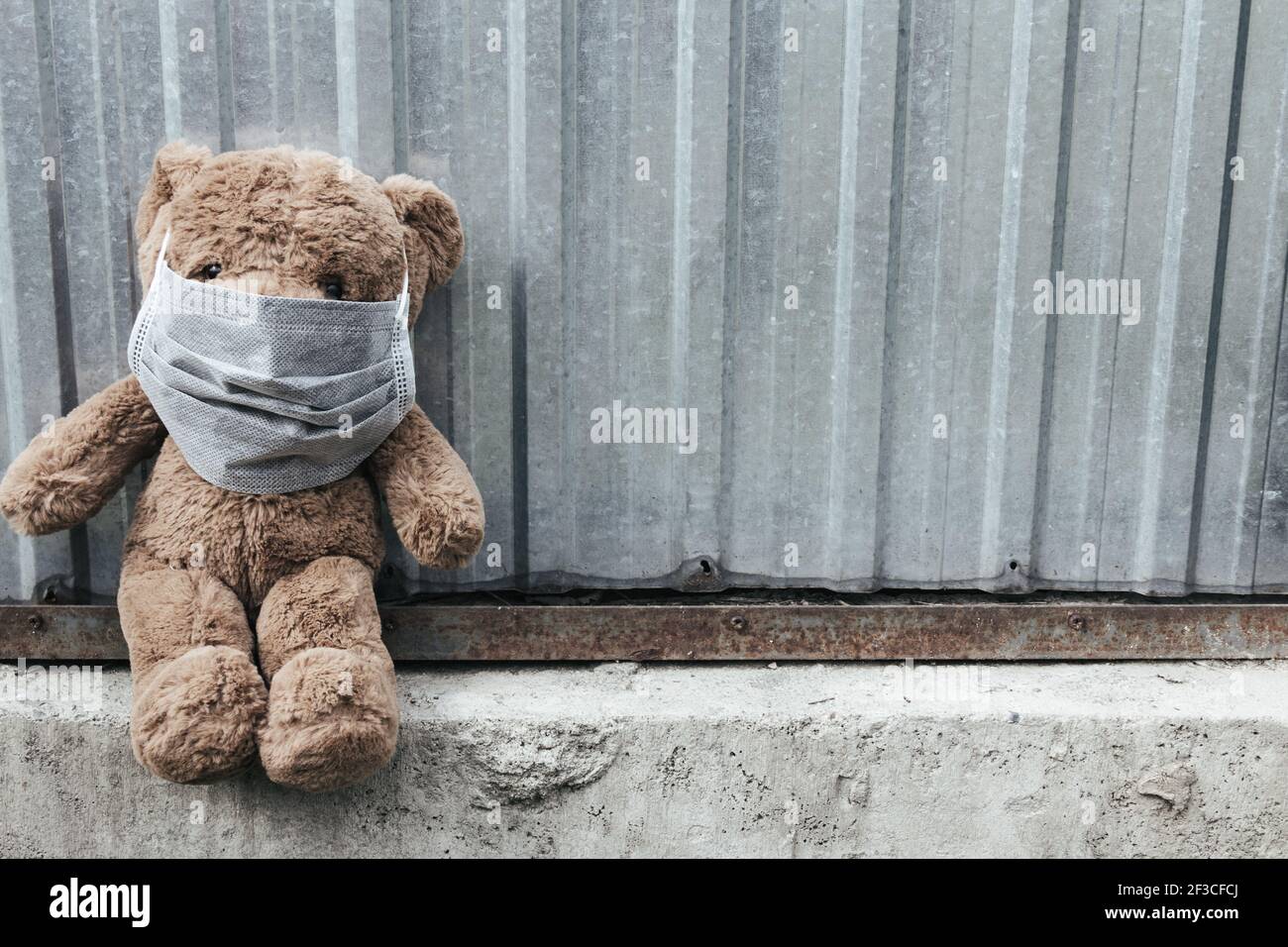 Teddybär in medizinischer Maske sitzt in der Nähe von Metallzaun. Traurige Emotionen über Quarantäne, Virus und Apokalypse Stockfoto