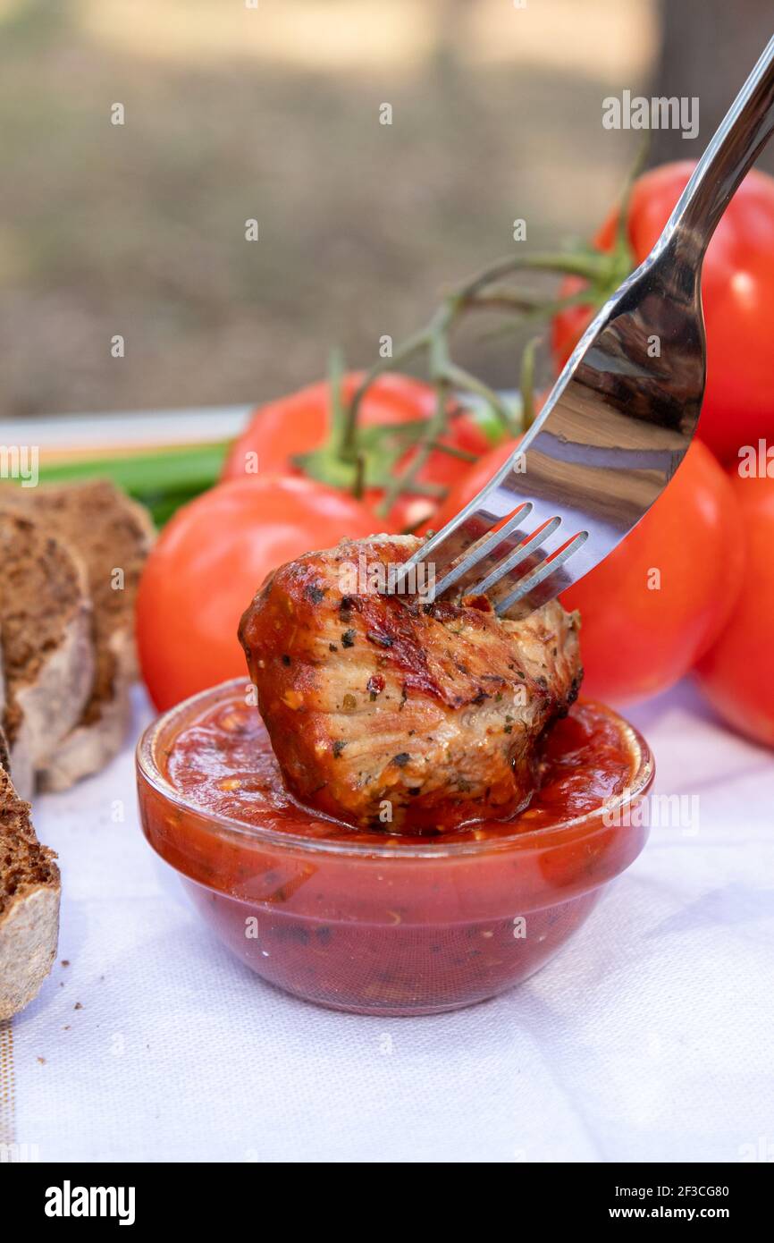 Hand mit einer Gabel taucht ein Stück Fleisch in rote Tomatensauce. Stockfoto