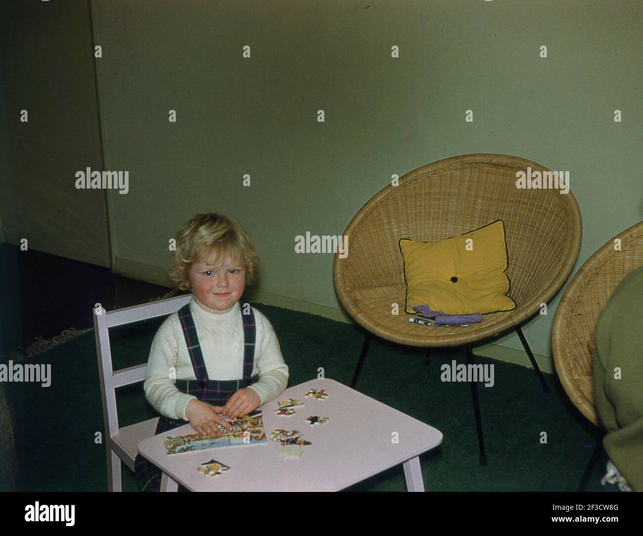 1960, historisch, in einem Raum, ein kleines Mädchen, das an einem kleinen rosafarbenen Kinderschreibtisch sitzt und ein Puzzle macht, England, Großbritannien. Puzzles waren ein wesentlicher Bestandteil der Kindheit in dieser Zeit und das Spielen mit Puzzles hat einen erheblichen Einfluss auf die körperlichen Fähigkeiten eines Kindes, die Entwicklung feinmotorischer Fähigkeiten durch den Einsatz kleiner Muskeln, was bedeutet, dass es einfacher ist, zu schreiben, zu zeichnen und Instrumente zu spielen. Durch das Zusammenfassen und Zusammenpassen von Puzzleteilen verbessern Kinder auch ihr räumliches Bewusstsein und die Hand-Auge-Koordination. Es gibt auch viele kognitive Vorteile des Spielens mit Puzzles. Stockfoto