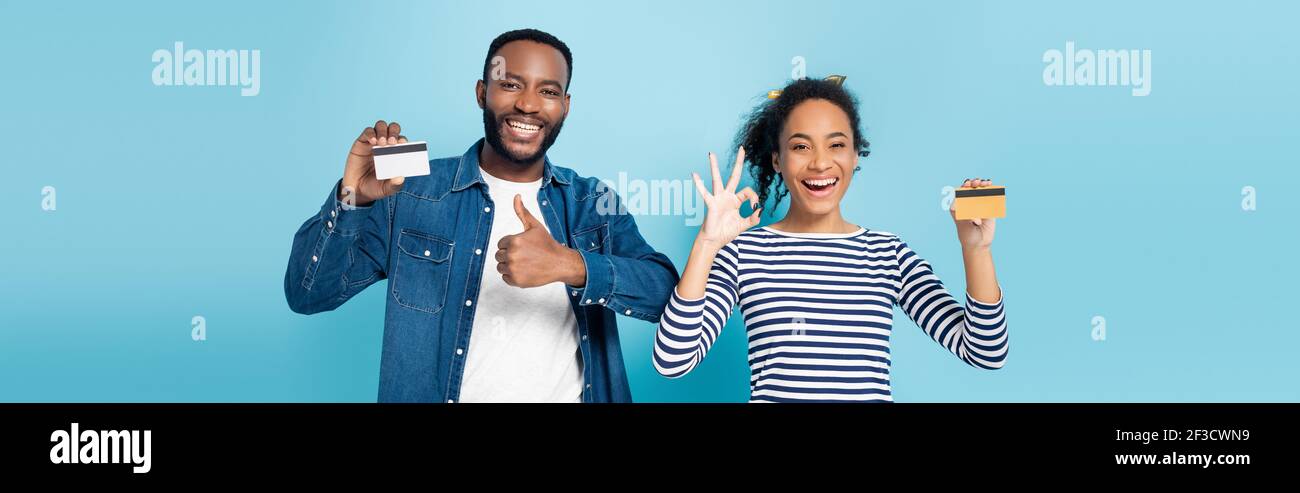 Aufgeregt afroamerikanischen Paar mit Kreditkarten und zeigt wie und okay Gesten auf blau, Banner Stockfoto