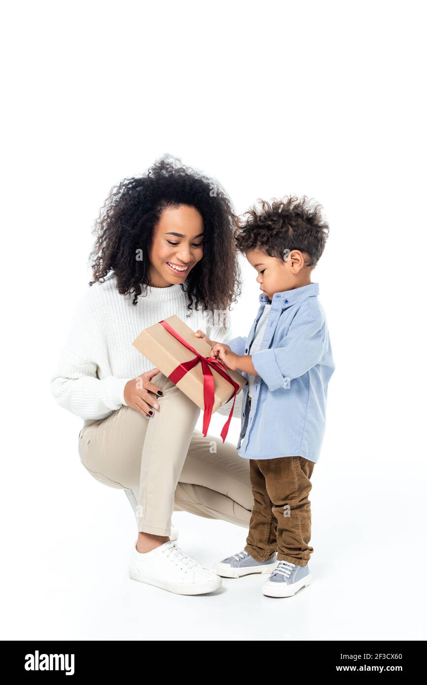 afroamerikanische Kinder Eröffnung Geschenkbox in der Nähe lächelnde Mutter auf Weiß Stockfoto