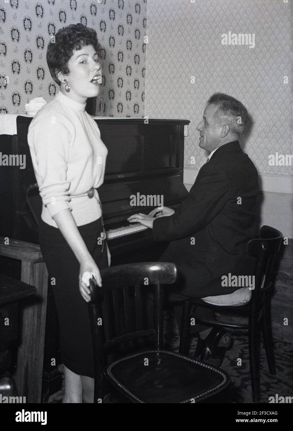 1957, historisch, in einer Hotel-Lounge-Bar, steht eine junge Dame, die ein Lied singt, während ein reifer Herr Klavier spielt, Leeds, England, Großbritannien. Stockfoto