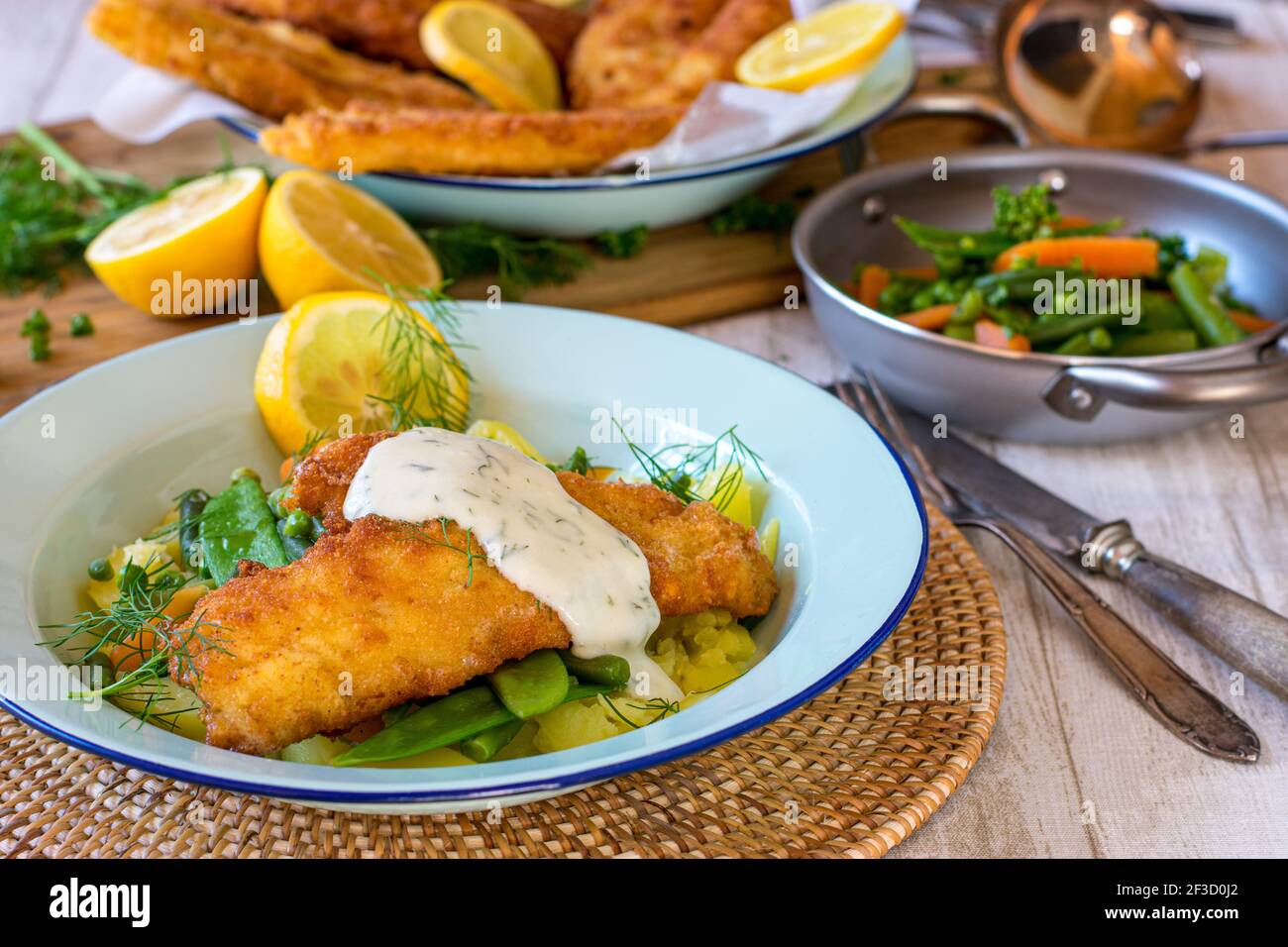 Fischgericht mit panierten Fisch, Gemüse, Kartoffeln und weißer Soße auf einem Teller Stockfoto