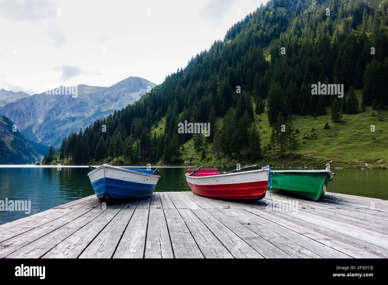 Drei Ruderboote liegen auf einer hölzernen Landebahn an einem idyllischen Bergsee in den alpen. Low-Angle-Ansicht, Vorderansicht. Stockfoto