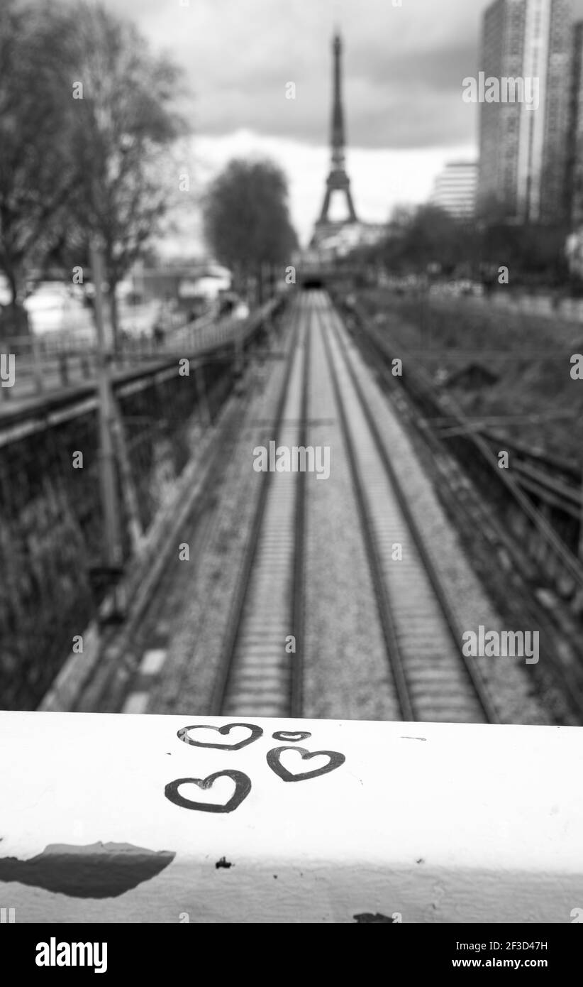 Pariser Stadtromantiker. Herzen auf dem Brückengeländer mit Blick Eisenbahn und Eiffelturm im Hintergrund. Schwarz weiß historisches Foto. Stockfoto