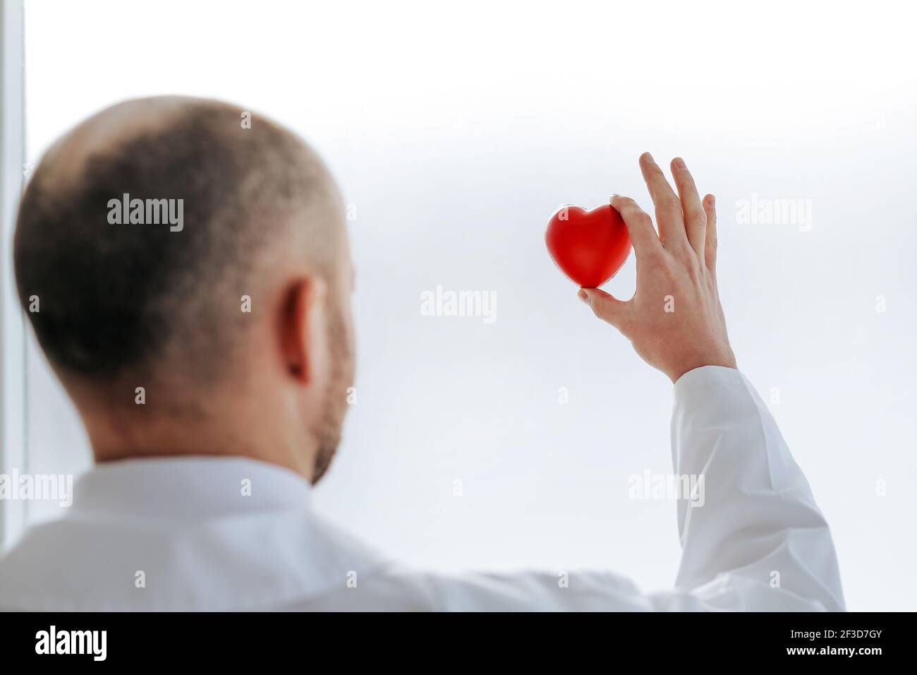 Doktor schaut auf das kleine rote Herz in seinen Händen. Stockfoto