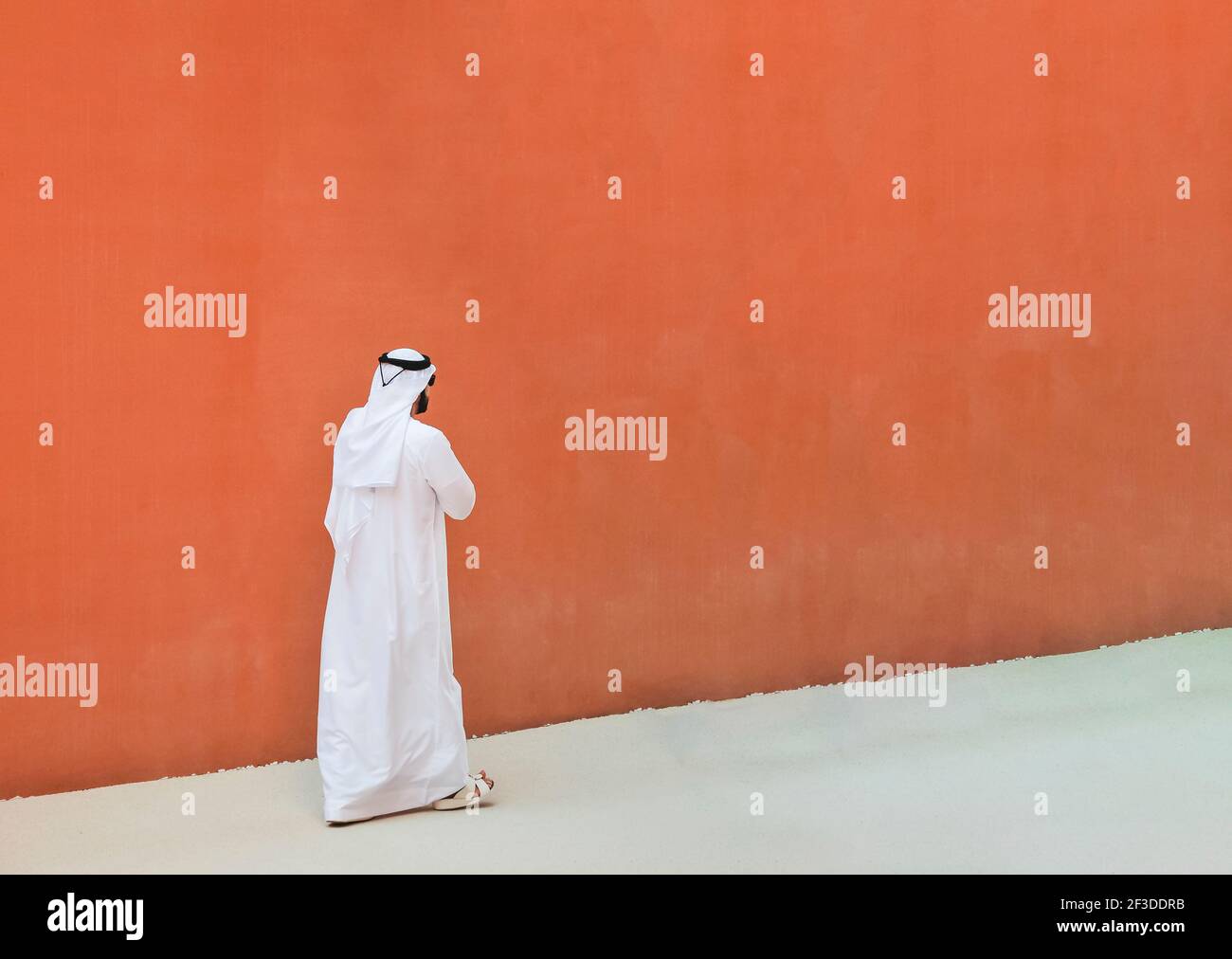 Arabischer Mann mit traditionellen emirates Kleidung zu Fuß im Freien in der Straße vor einer orangefarbenen Wand Hintergrund - arabische Ethnie und muslimische Religion Konz Stockfoto