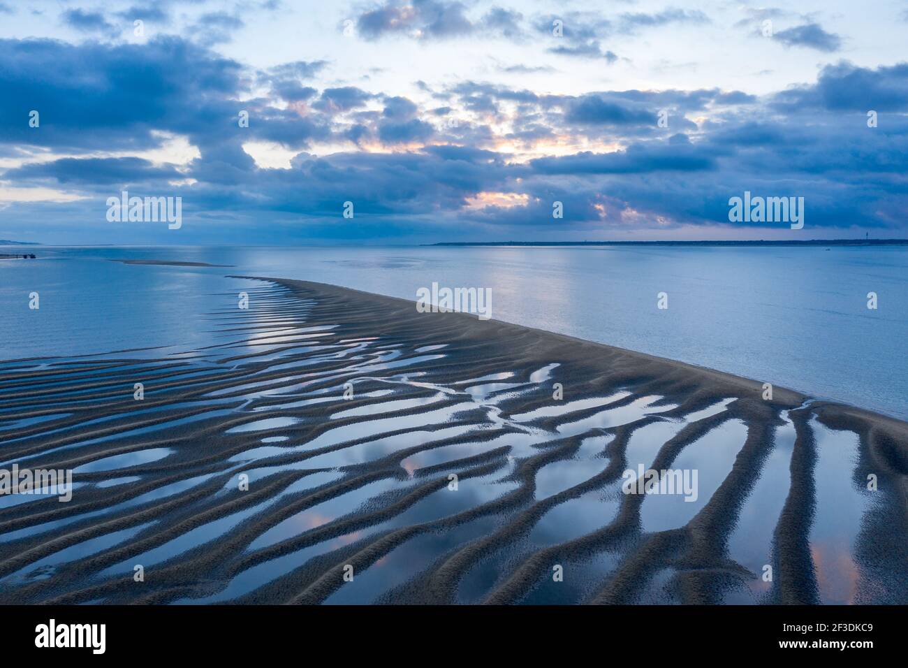 Bei Ebbe Blick auf die Küste. Viele Wasserlagunen bleiben am Strand hinter Sanddeichen. Farbenfroher Himmel mit Wolken nach Sonnenuntergang. Stockfoto