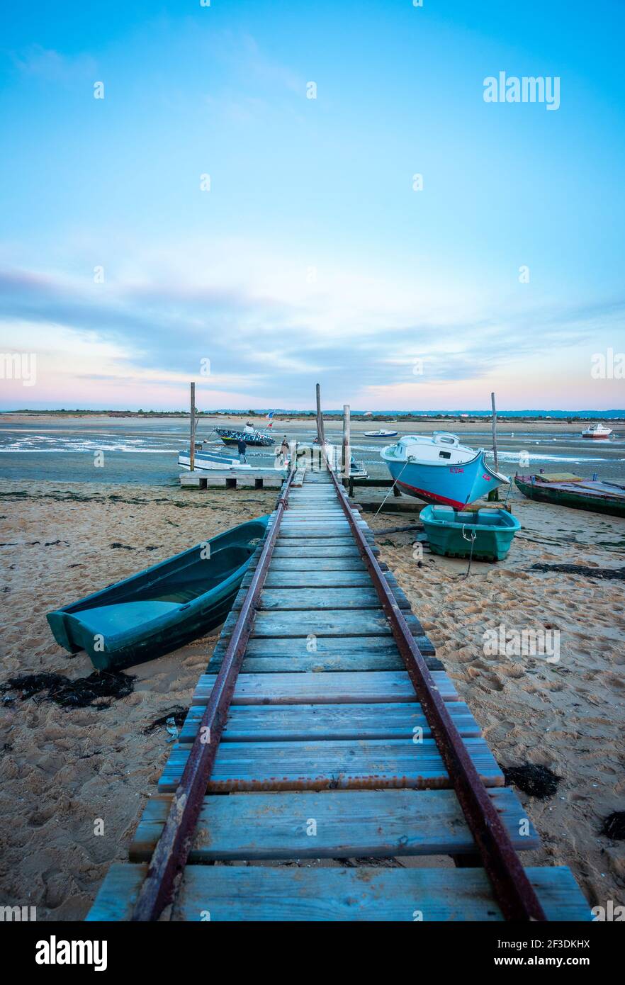 Schienen, die mit einer hölzernen Plattform verbunden sind, die zum Abstoßen von Booten auf das Wasser verwendet wird. Mehrere Boote am Strand bei Ebbe. Stockfoto
