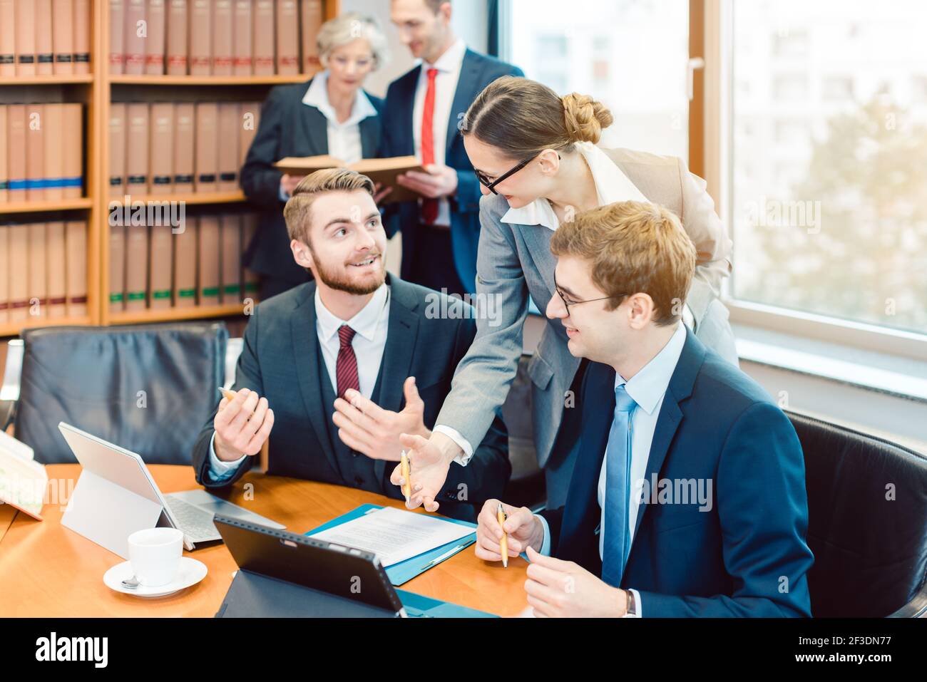 Rechtsanwälte in ihrer Kanzlei, die mit Büchern im Hintergrund am Computer arbeiten Stockfoto