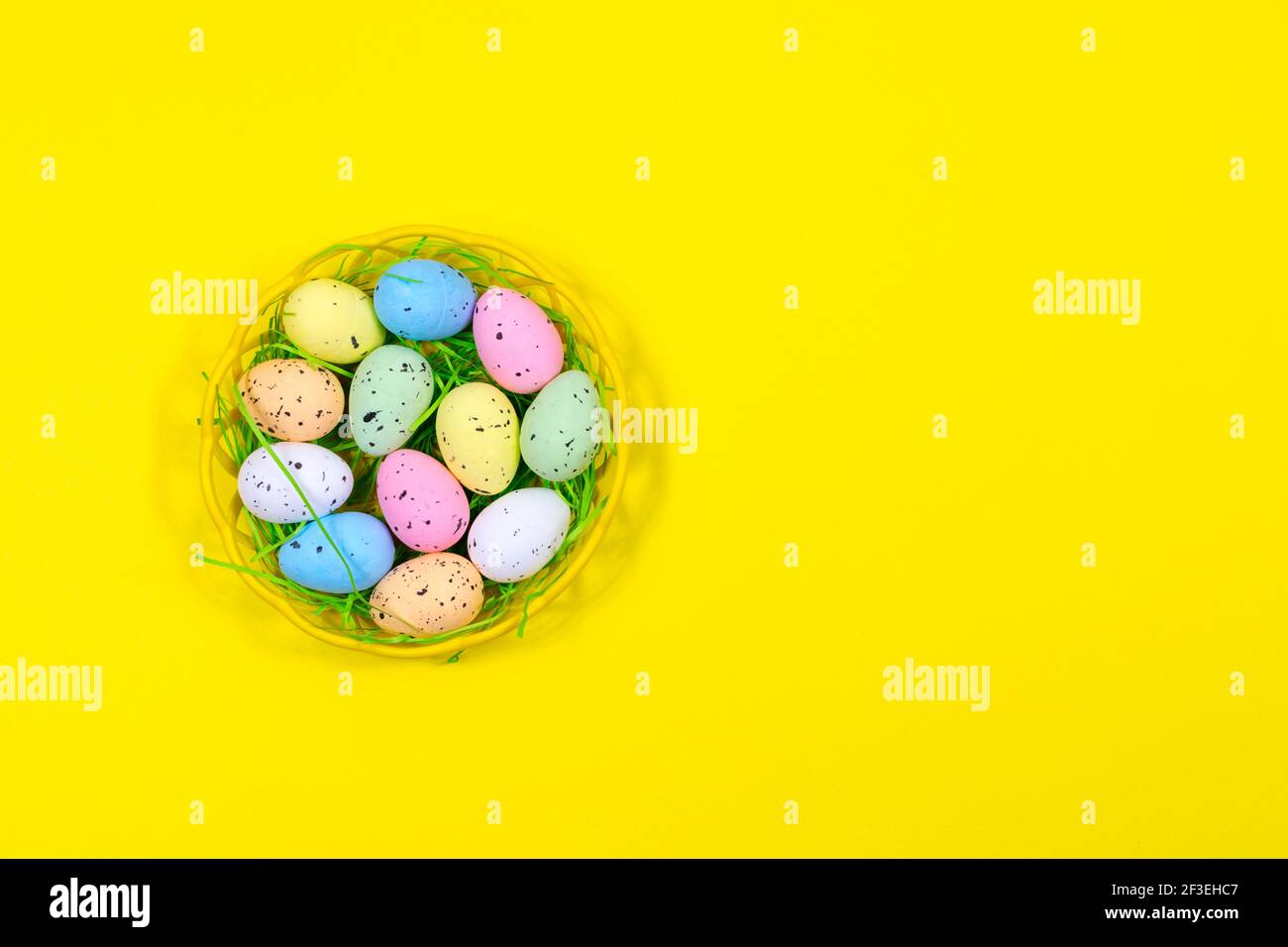 Bunte Ostereier in einer Schale auf gelbem Hintergrund. Platz für eine Inschrift. Blick von oben. Ostern. Stockfoto