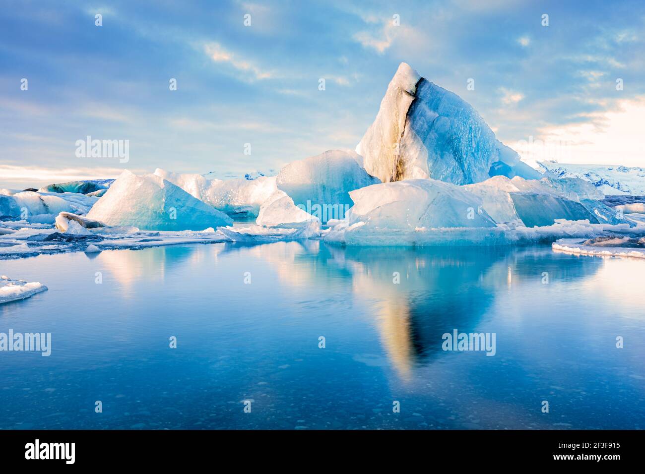 Eisberge schweben auf der Jokulsarlon Gletscherlagune mit Berggipfeln, die vom warmen Sonnenaufgangslicht beleuchtet werden, in Island. Stockfoto