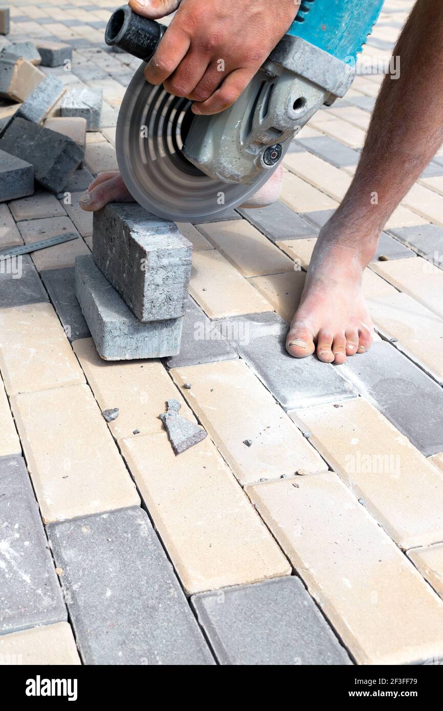 Ein Arbeiter schneidet Pflasterplatten mit einer Mühle für die anschließende Verlegung, vertikalen Schuss. Stockfoto