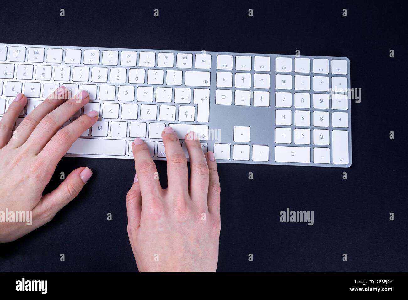 Weibliche Hände auf der weißen Tastatur auf schwarzem Grund. Schreiben, Schreiben, freiberuflich und Arbeiten von der Heimtastatur. Stockfoto