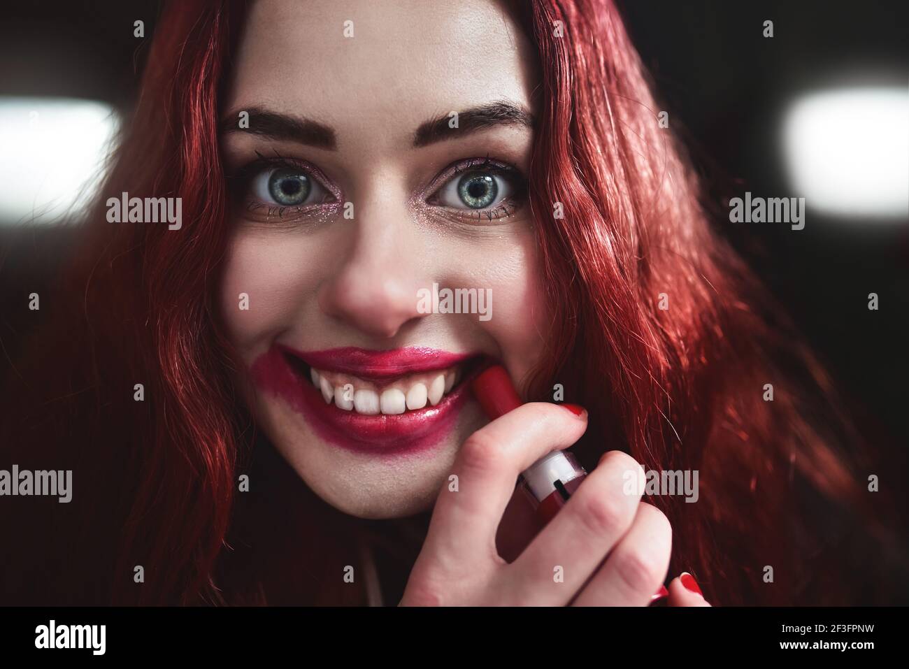 Porträt von verrückt aussehende Teenager-Mädchen mit roten Haaren ist sie schmieren roten Lippenstift auf ihrem Gesicht, Horror-Konzept. halloween-Zeit. Angst und Alptraum Stockfoto
