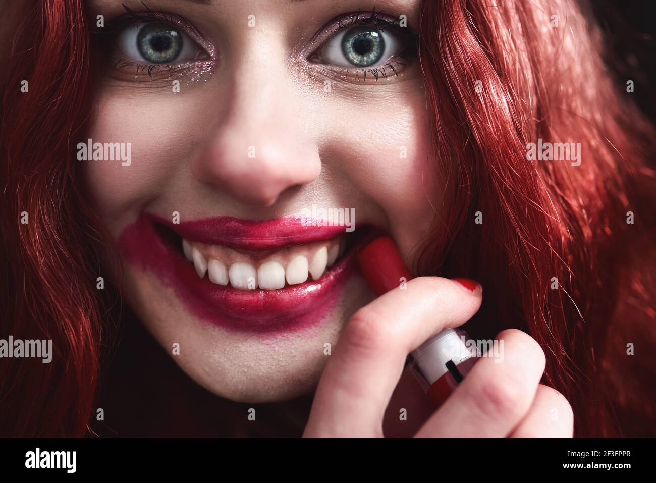 Porträt von verrückt aussehende Teenager-Mädchen mit roten Haaren ist sie schmieren roten Lippenstift auf ihrem Gesicht, Horror-Konzept. halloween-Zeit. Angst und Alptraum. Nahe Stockfoto