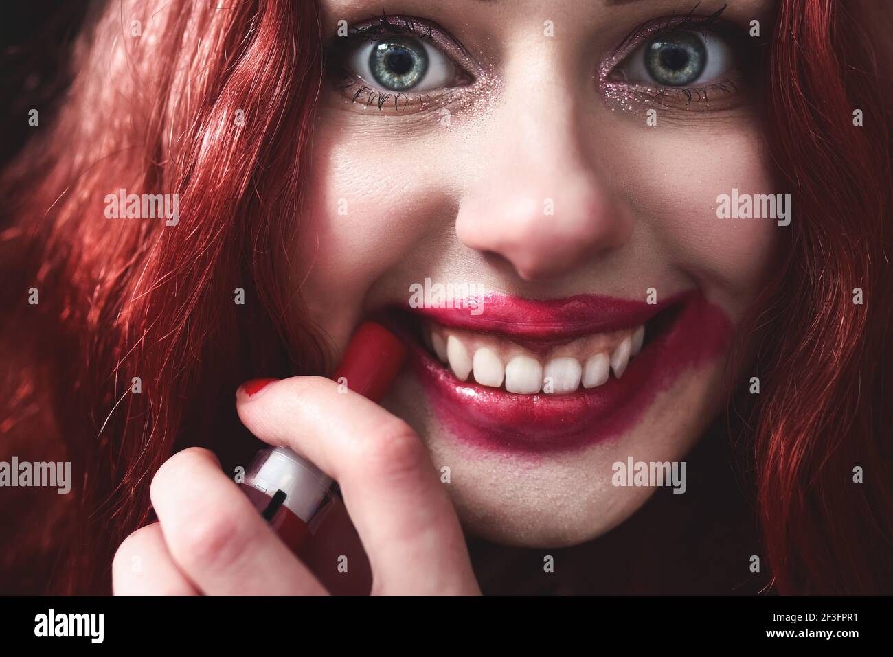 Porträt von verrückt aussehende Teenager-Mädchen mit roten Haaren ist sie schmieren roten Lippenstift auf ihrem Gesicht, Horror-Konzept. halloween-Zeit. Angst und Alptraum. Nahe Stockfoto