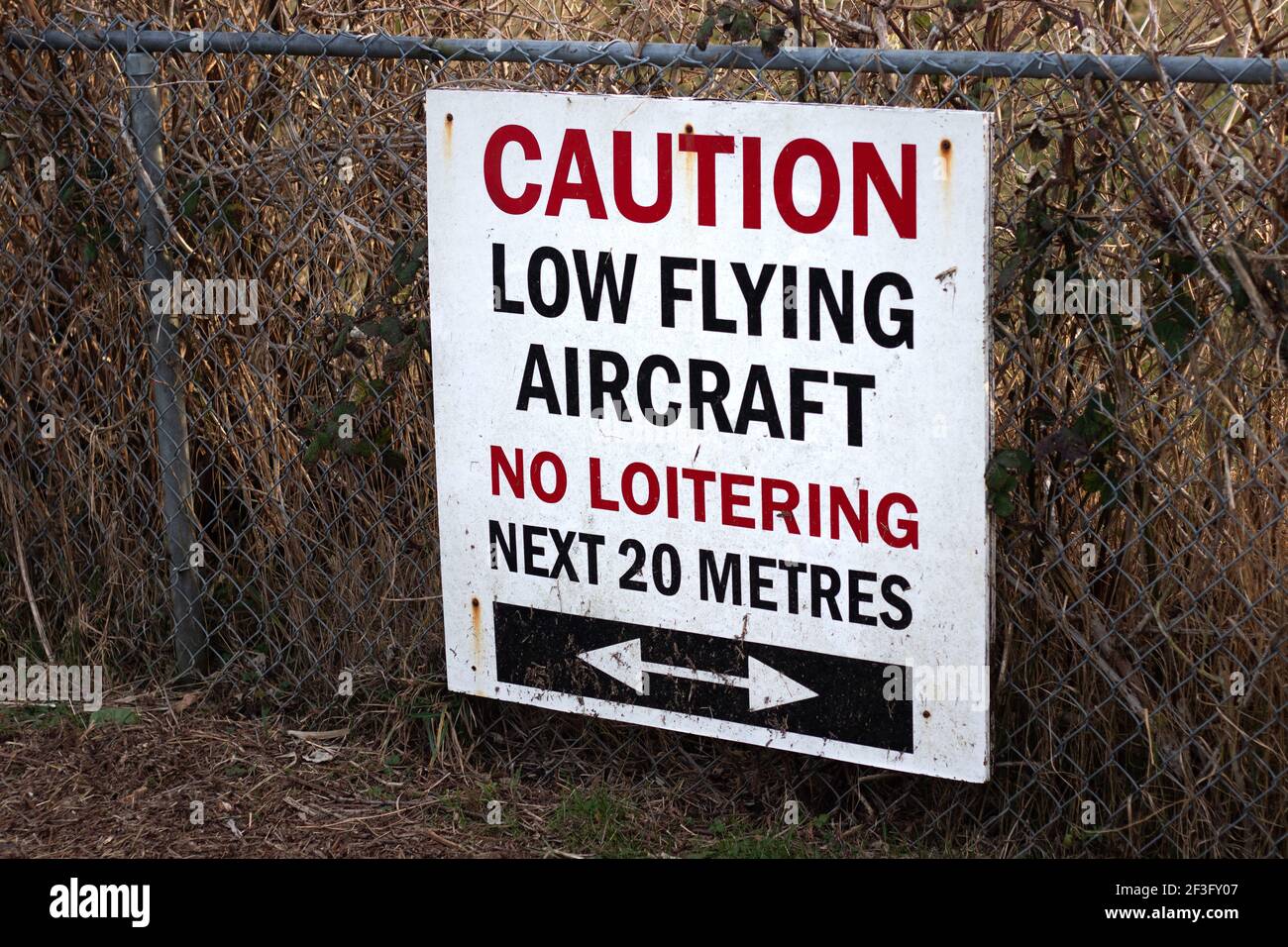 Blick auf Schild Vorsicht Low Flying Aircraft, No loitering Nächste 20 Meter am lokalen Flughafen in Courtenay, Kanada Stockfoto