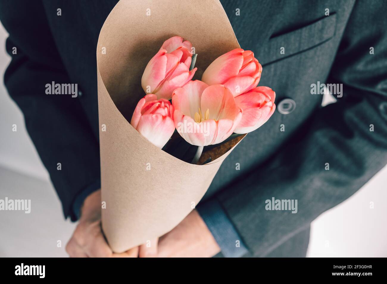 Eleganter Mann mit einem Bouquet aus rosa Tulpen, eingewickelt in Bastelpapier. Überraschung für Ihre geliebte Frau. Romantisches Kurzurlaub-Konzept. Selektiver Fokus. Stockfoto