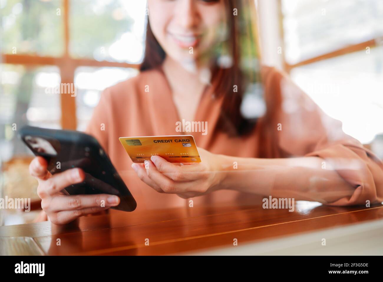 Asiatische Frau hält Bankkreditkarte für die Zahlung auf dem Smartphone Für Online-Shopping sitzen im Café mit Glas für soziale Distanzierung während covid-19 Stockfoto