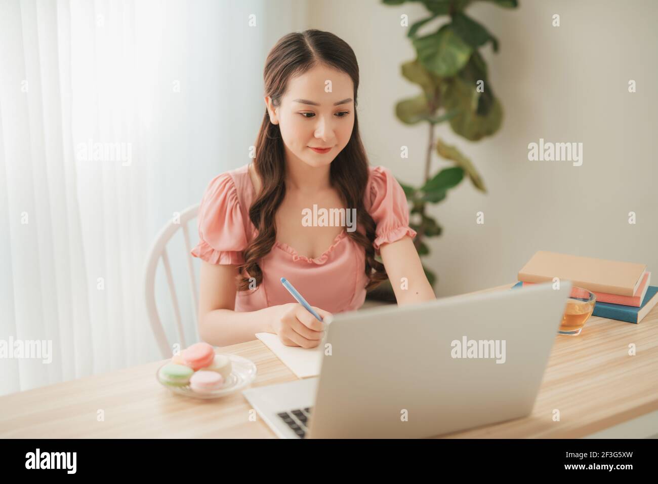 Lächelnde asiatische Frau arbeitet mit Laptop auf Tisch in weiß Home Office im Innenbereich Stockfoto