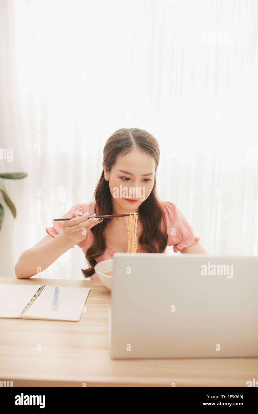 Weibliche Angestellte hält Essstäbchen essen Instant Nudel am Arbeitsplatz in Heimbüro Stockfoto