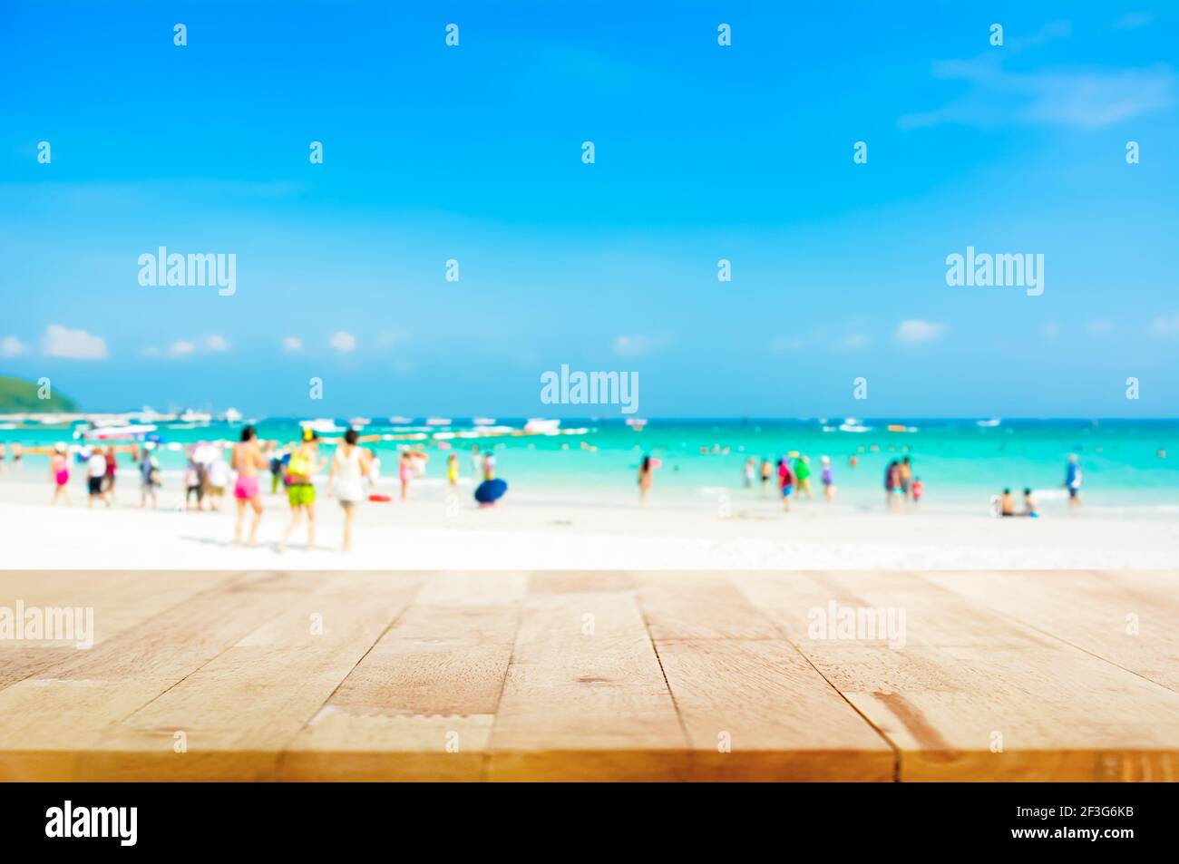 Holztischplatte auf verschwommenem Strand Hintergrund mit Menschen in Bunte Kleidung - kann für die Anzeige oder Montage verwendet werden Ihre Produkte Stockfoto