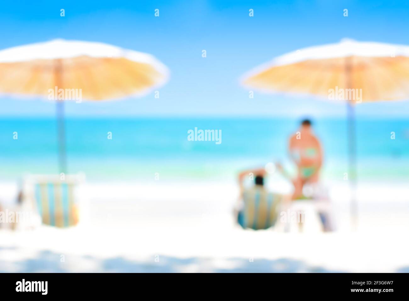 Verschwommenes blaues Meer und weißer Sandstrand mit Sonnenschirmen, Liegestühlen und einigen Menschen - Sommer- und Urlaubshintergrundkonzepte Stockfoto