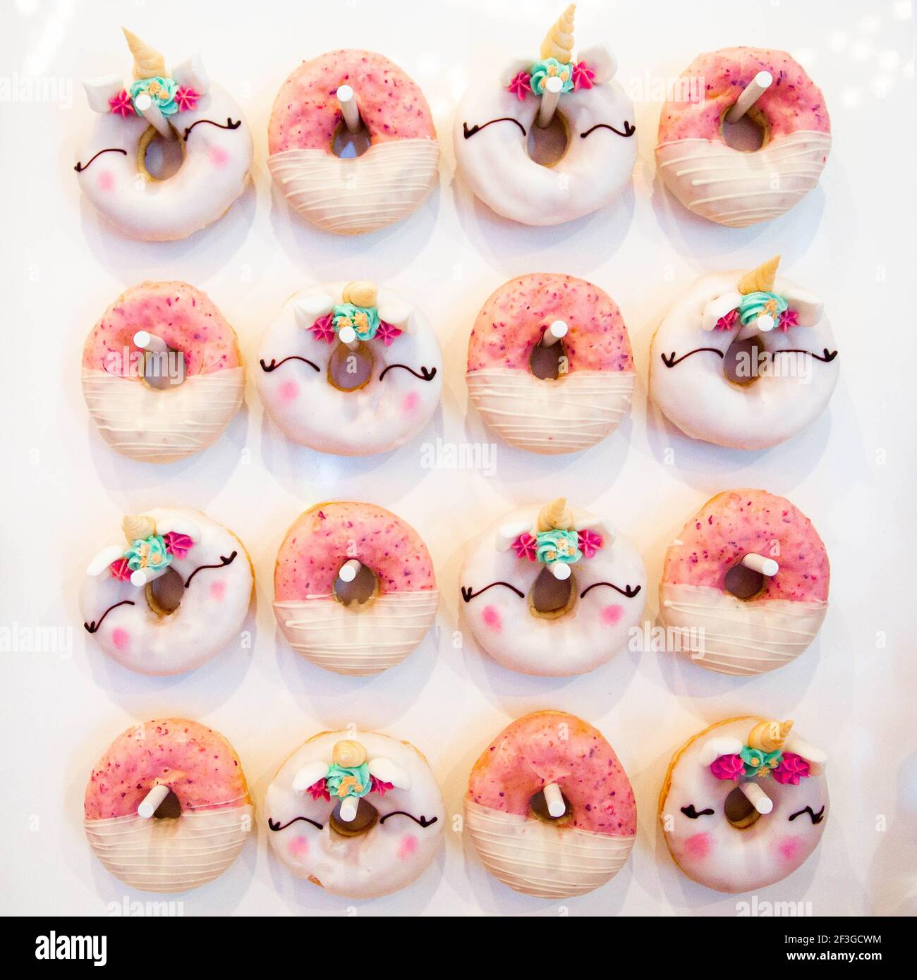 Ein Satz Donuts, Reihe 4 von 4. Pink gestreifte Donuts und Einhorn-Donuts hängen an Haken im Schachbrettmuster auf weißem Hintergrund Stockfoto