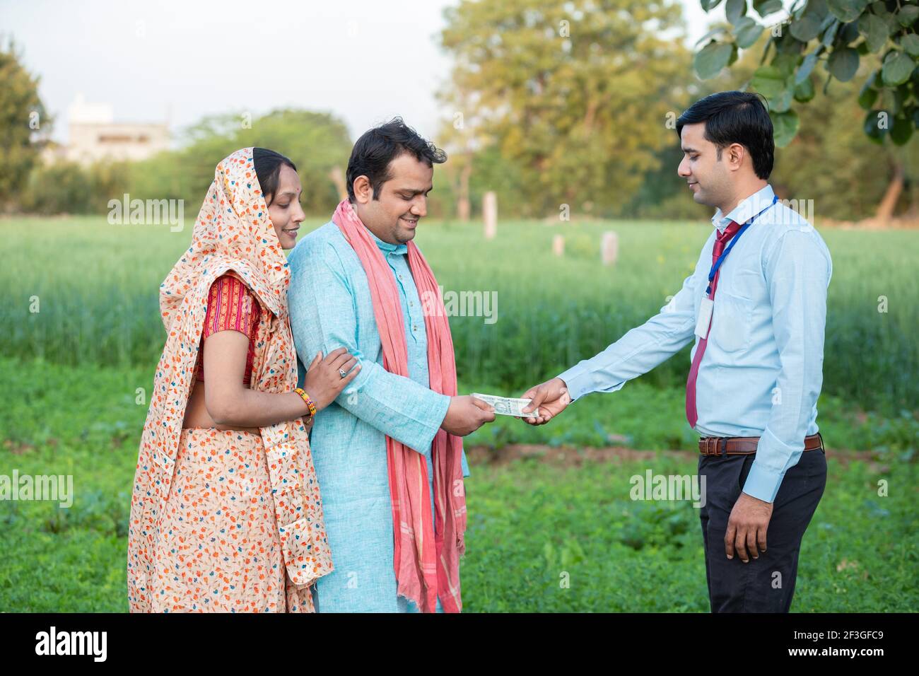 Junge ländliche indische Paar Farmer erhalten Geld von Bankier auf Landwirtschaft Feld. Stockfoto