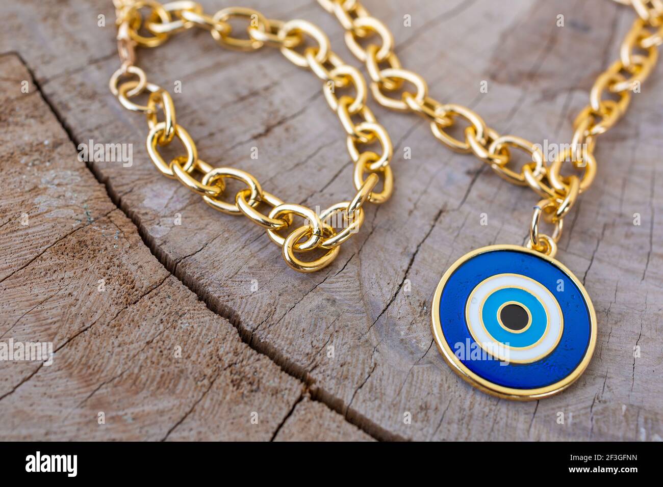 Eine Nahaufnahme einer goldenen Kette Halskette mit einem Blauer Bullseye-Anhänger auf einer Holzoberfläche Stockfoto
