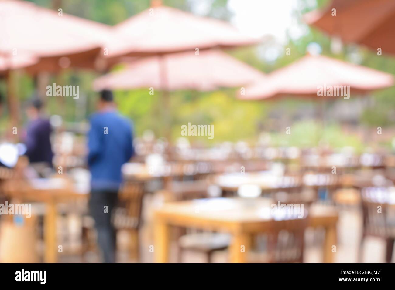 Verschwommenes Bild als Hintergrund eines Restaurants im Freien mit Tischen, Stühlen und Sonnenschirmen Stockfoto