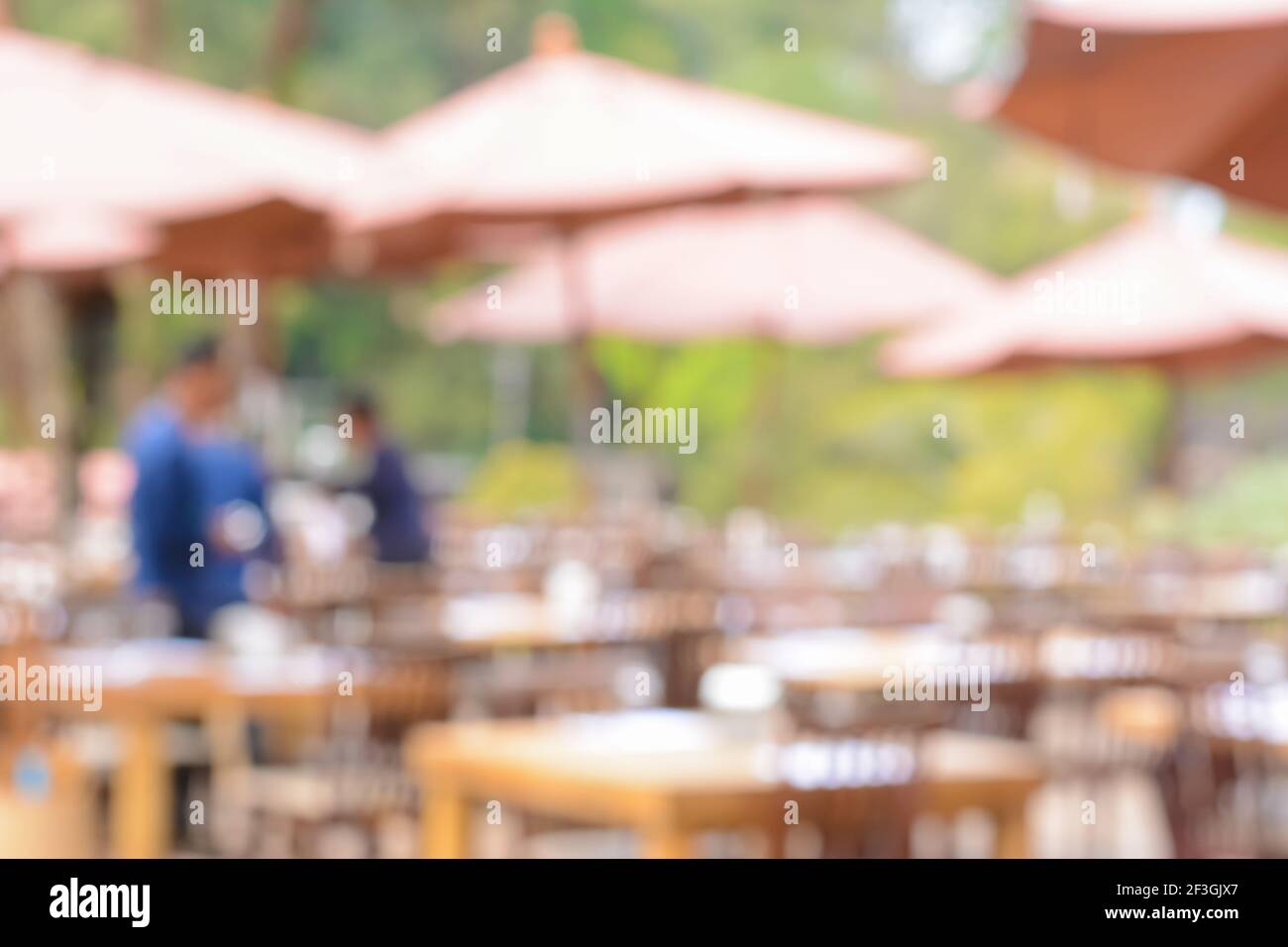 Verschwommenes Bild als Hintergrund eines Restaurants im Freien mit Tischen, Stühlen und Sonnenschirmen Stockfoto