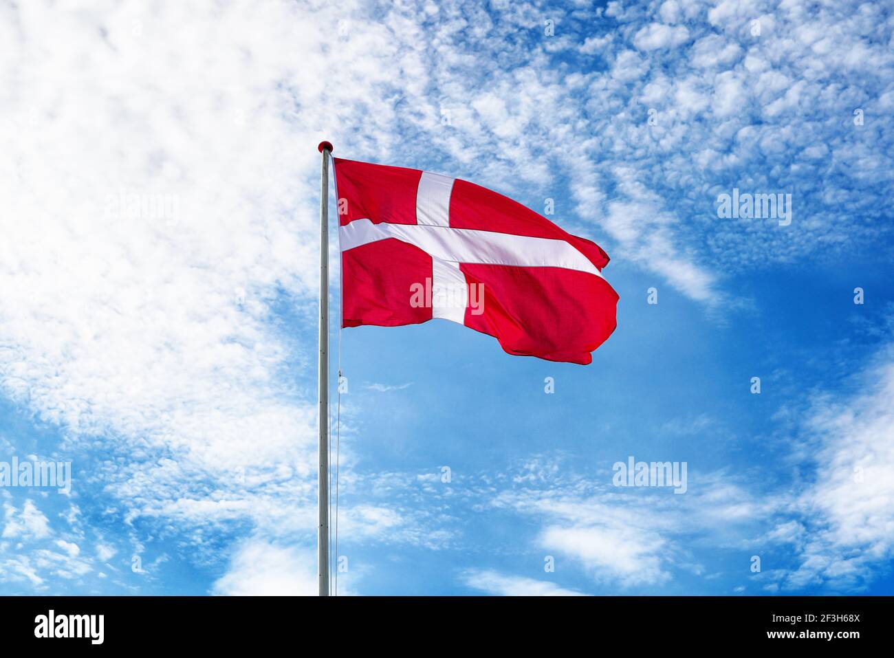 Dänische Flagge am blauen Himmel. Flagge Dänemarks winkt im Wind. Helles und buntes Konzept für Reisen und Tourismus. Stockfoto