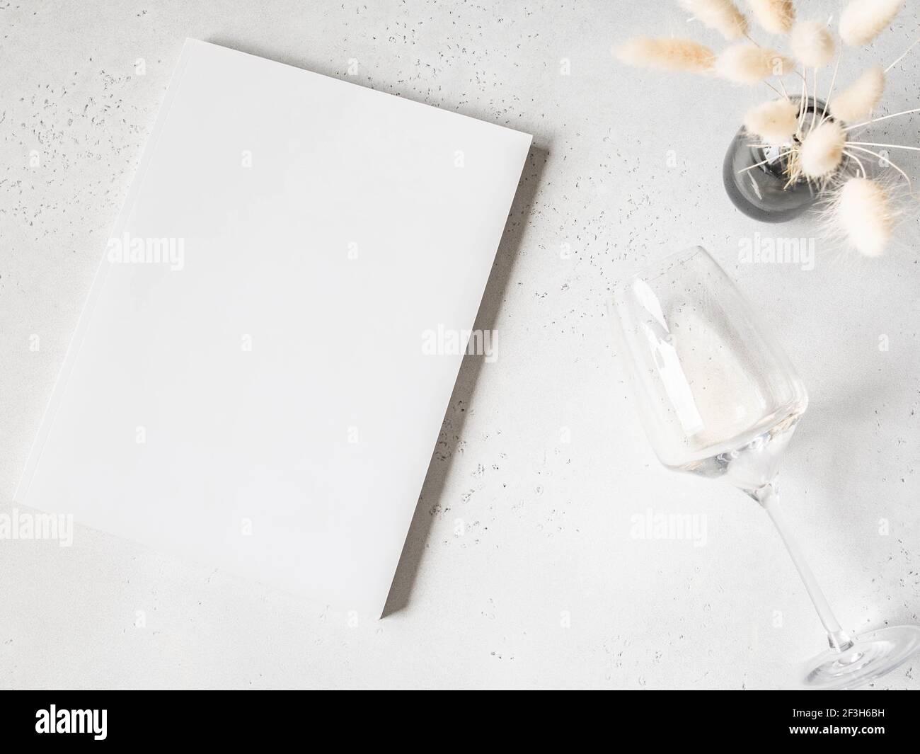 Weißer Zeitschriftendeckel Mockup, weißer Lagurus in Vase und Glas Weißwein auf hellgrauem Hintergrund. Draufsicht. Speicherplatz kopieren Stockfoto
