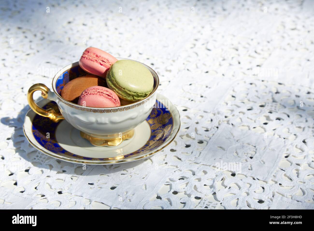 Makronen Kekse in rosa, grün und braun Farben mit Keramik blau und golden Tasse und weiß bestickte Tischdecke Stockfoto