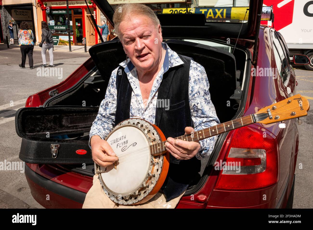 Der irische Taxifahrer sitzt im Kofferraum seines Autos und spielt ein Banjo, das am College Street Taxistand in Killarney, County Kerry, Irland, auf Fahrpreise wartet Stockfoto