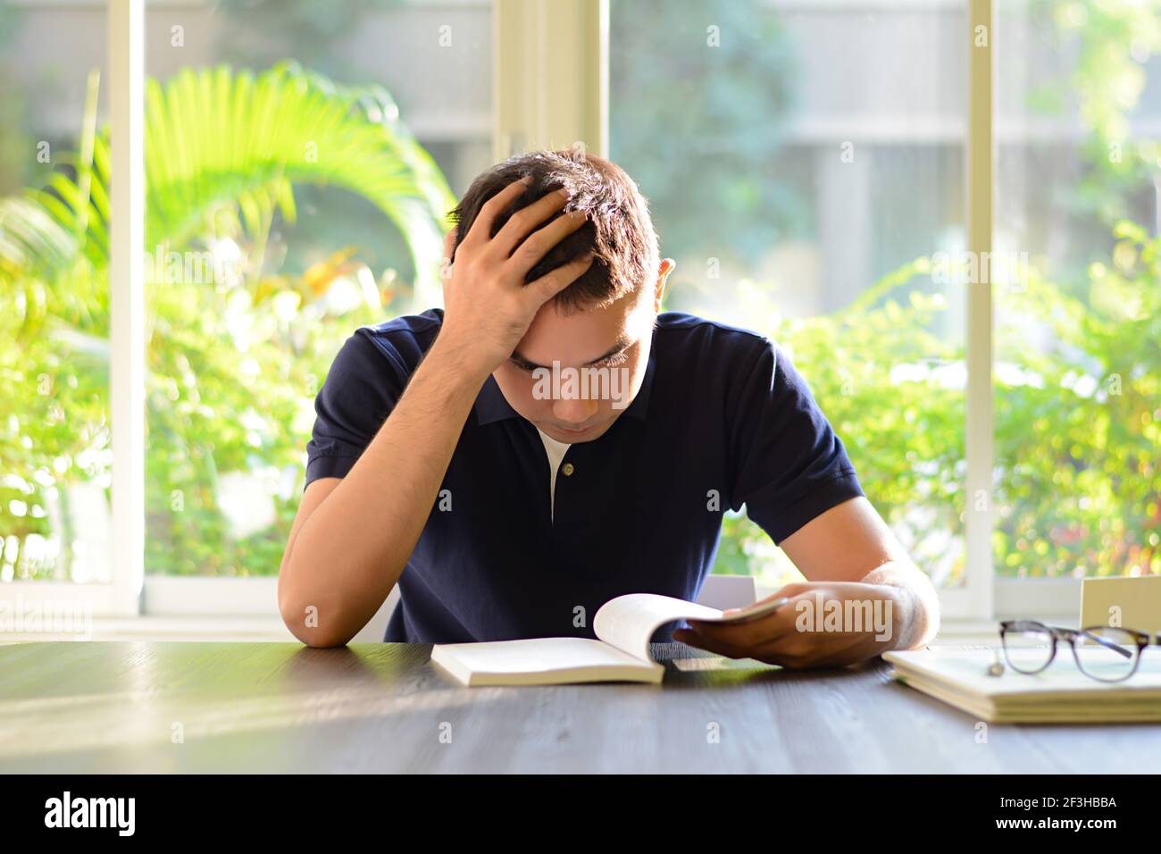 Gestresster Mann liest Buch mit der Hand auf dem Kopf - Studien- & Prüfungskonzepte Stockfoto