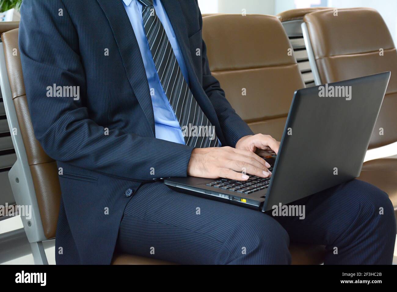 Geschäftsmann mit Laptop oder Notebook-Computer, während er auf dem sitzt Stuhl am Flughafen Stockfoto