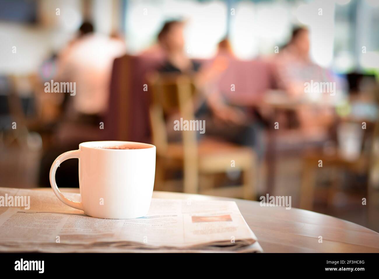 Kaffeetasse über Zeitung auf dem Tisch mit den Leuten Café als Hintergrund verwacklungsunscharf Stockfoto