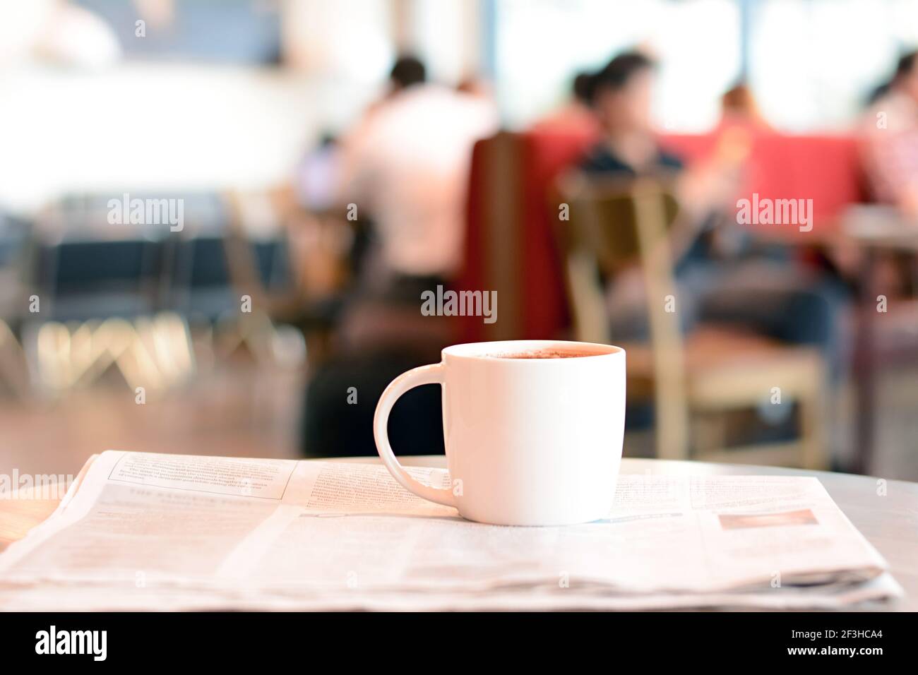 Kaffeetasse über Zeitung auf dem Tisch mit den Leuten Café als Hintergrund verwacklungsunscharf Stockfoto