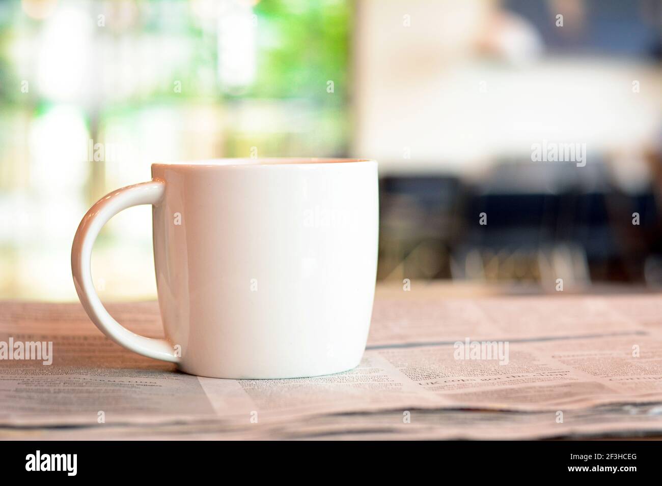 Kaffeetasse über Zeitung auf dem Tisch in verschwommenem Kaffee Shop-Hintergrund Stockfoto
