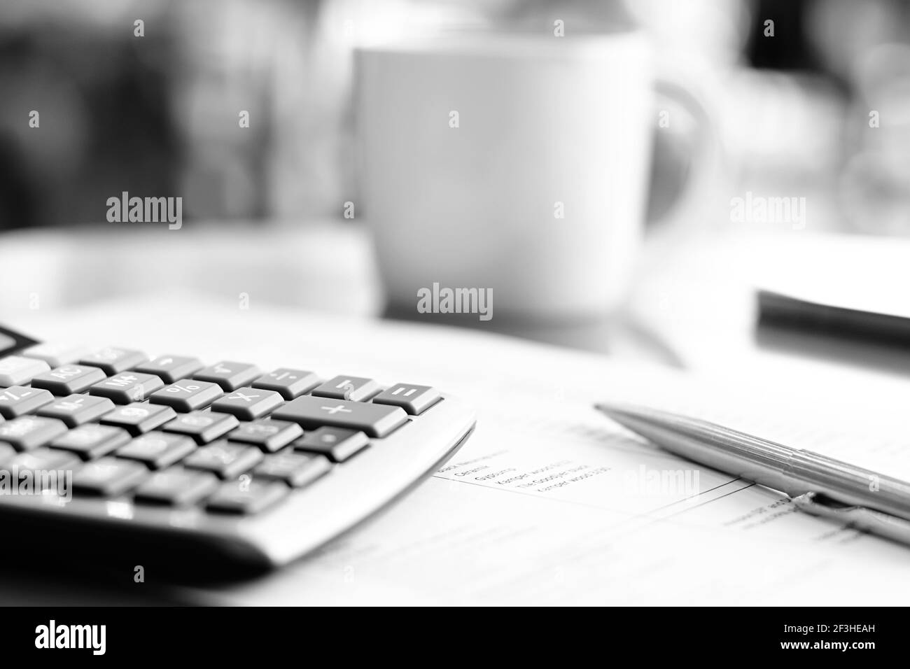 Taschenrechner & Stift über Papier auf dem Tisch mit Unschärfe Kaffeetasse Hintergrund - monochromer Effekt Stockfoto