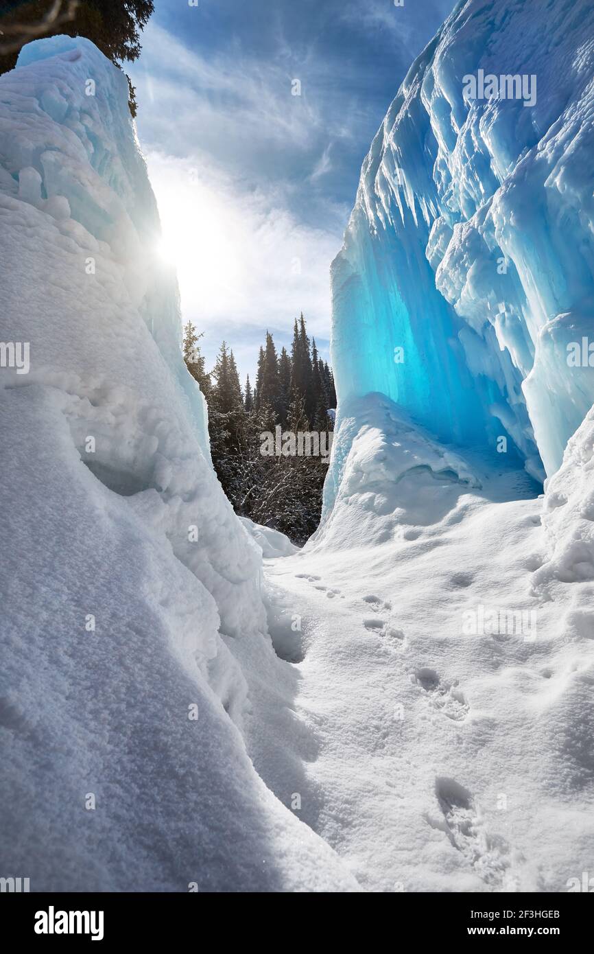 Gefrorener Bergwasserfall mit Eiszapfen gegen blauen Himmel und Wald Im Hintergrund Stockfoto
