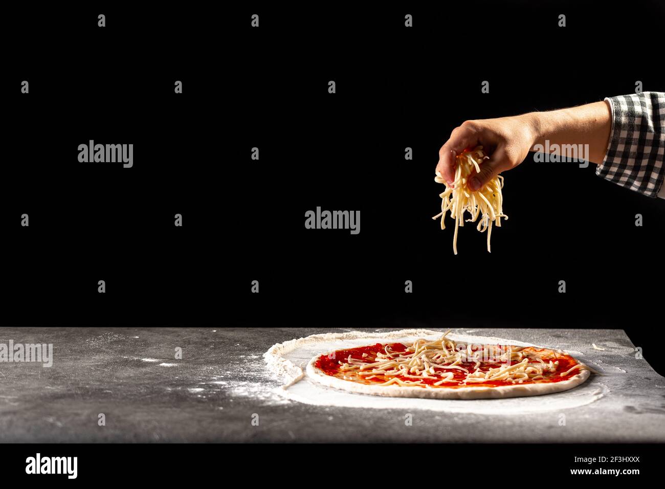 Eine Pizza machen, Teig mit Käse bestreuen Stockfoto
