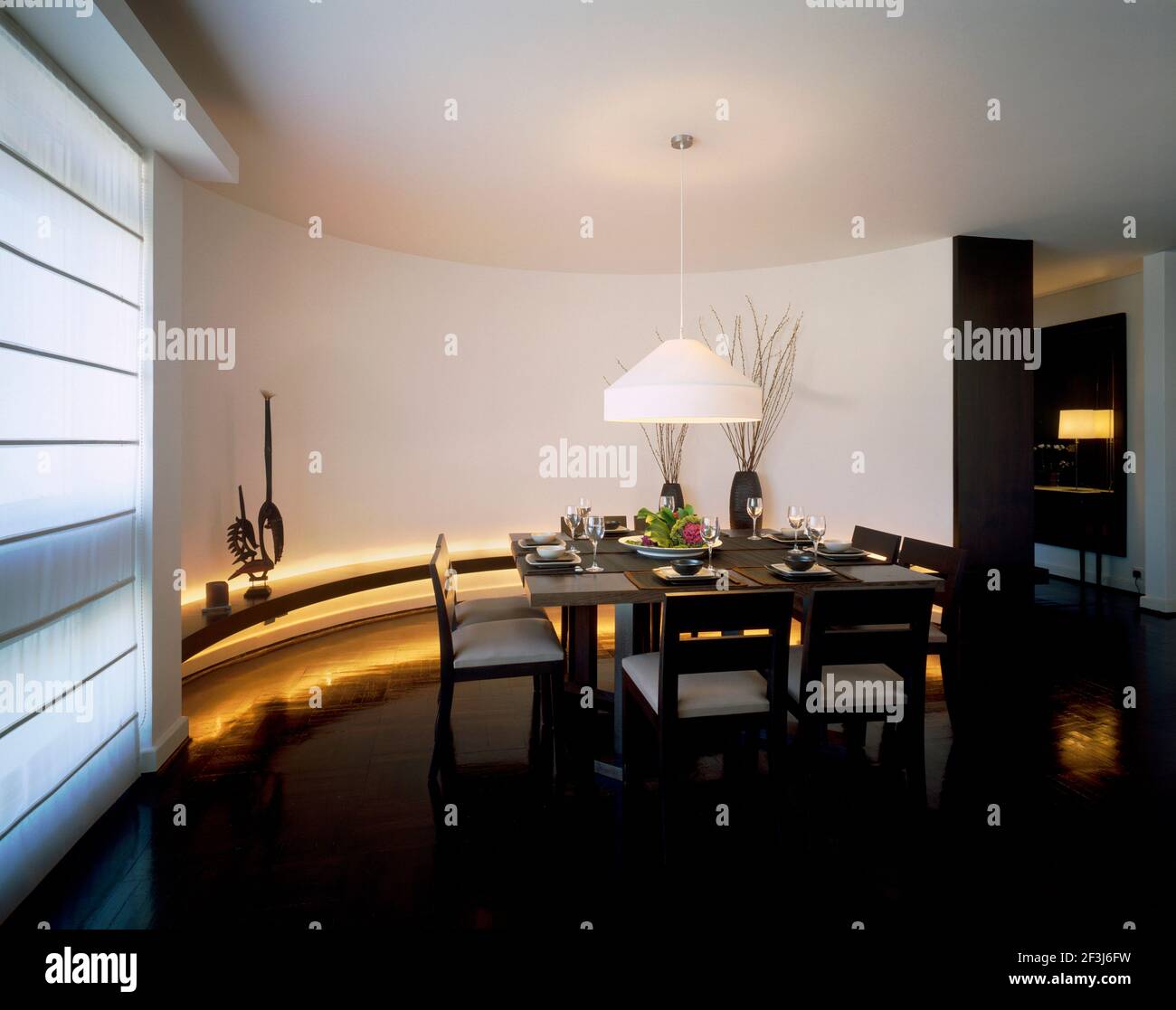 Die geometrischen und einfachen Linien einer quadratischen Tabelle in Wenge Holz mit Stühlen von Christian Liaigre werden durch versetzt Die geschwungene Wand in diesem zeitgenössischen Kow Stockfoto