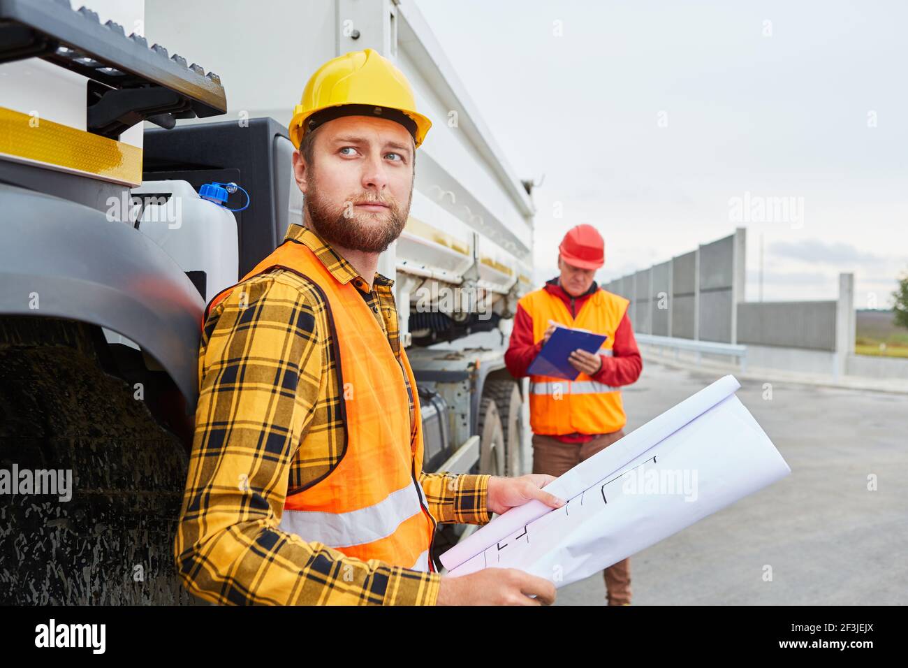 Arbeiter mit Bauzeichnung oder Lageplan vor Ein LKW mit Baustoffen für die Baustelle Stockfoto