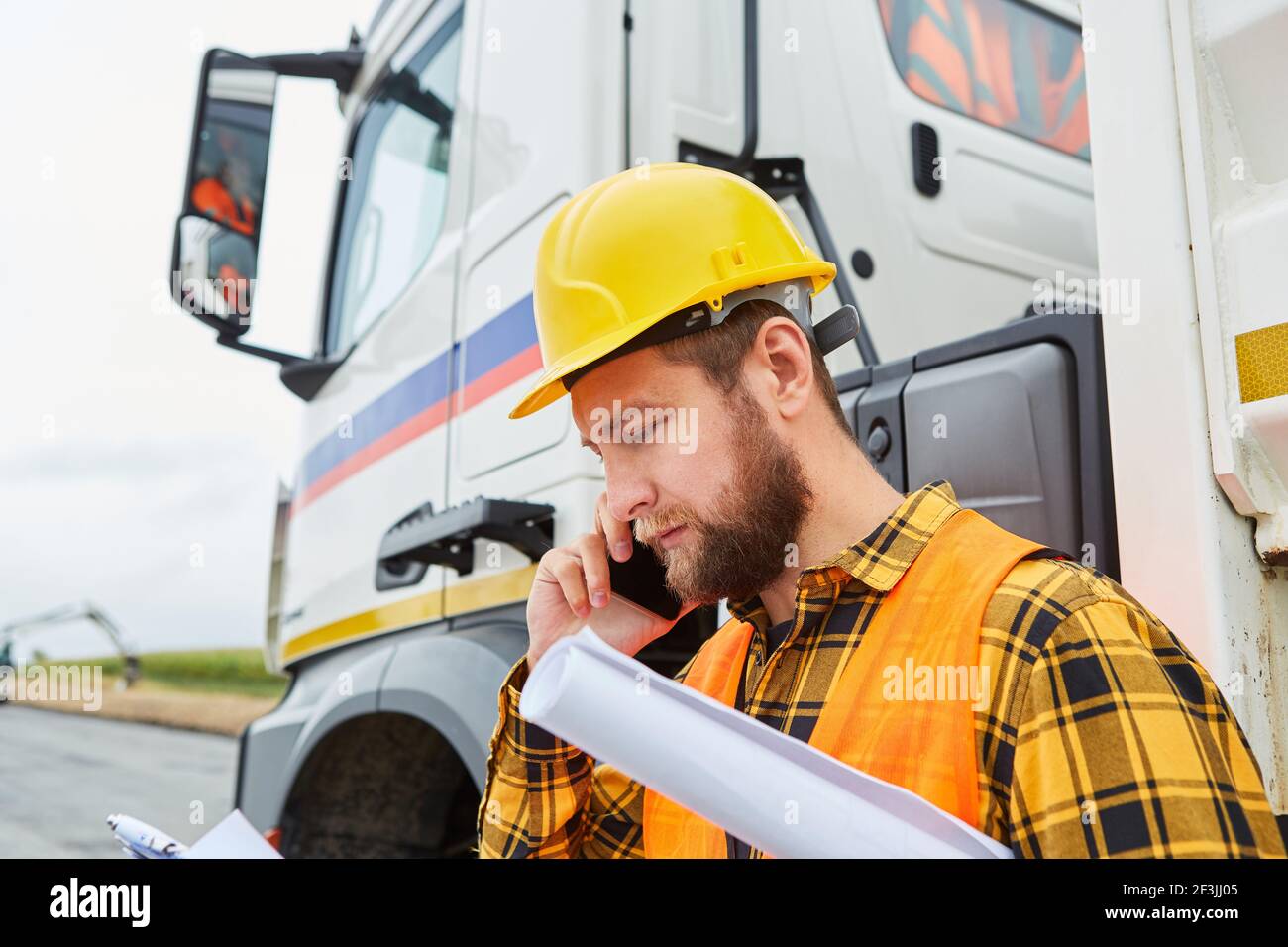 Bauarbeiter ruft vor einem LKW mit Mobile Telefon auf der Baustelle des Straßenbaus Stockfoto