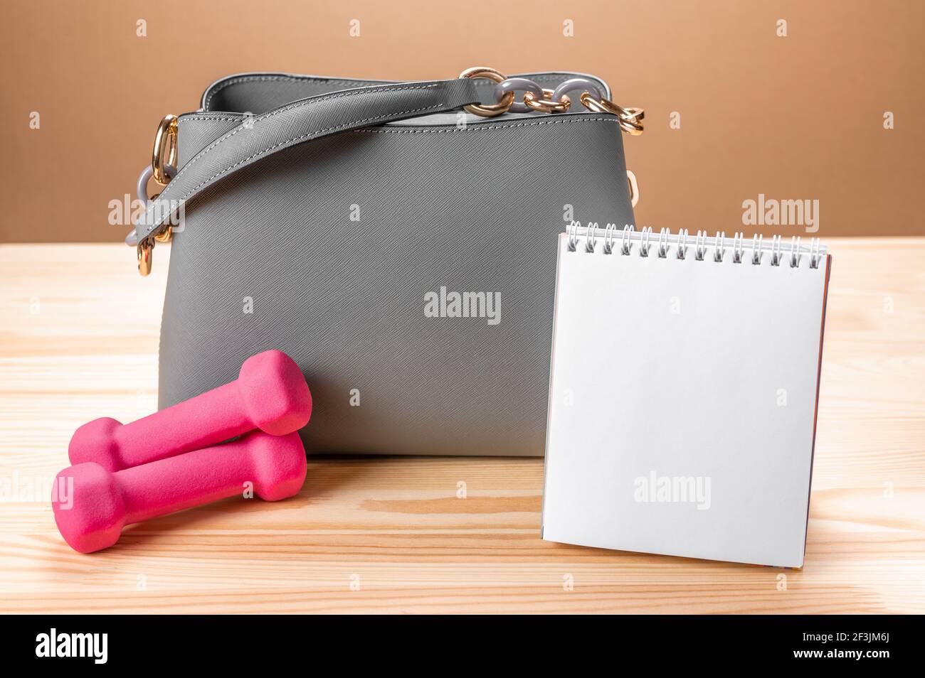 Damen Leder graue Handtasche, Notizblock und kleine rosa Hanteln. Damentasche und Notizblock zum Schreiben und Fitness-Hanteln. Konzept Zeitplan Training, pl Stockfoto