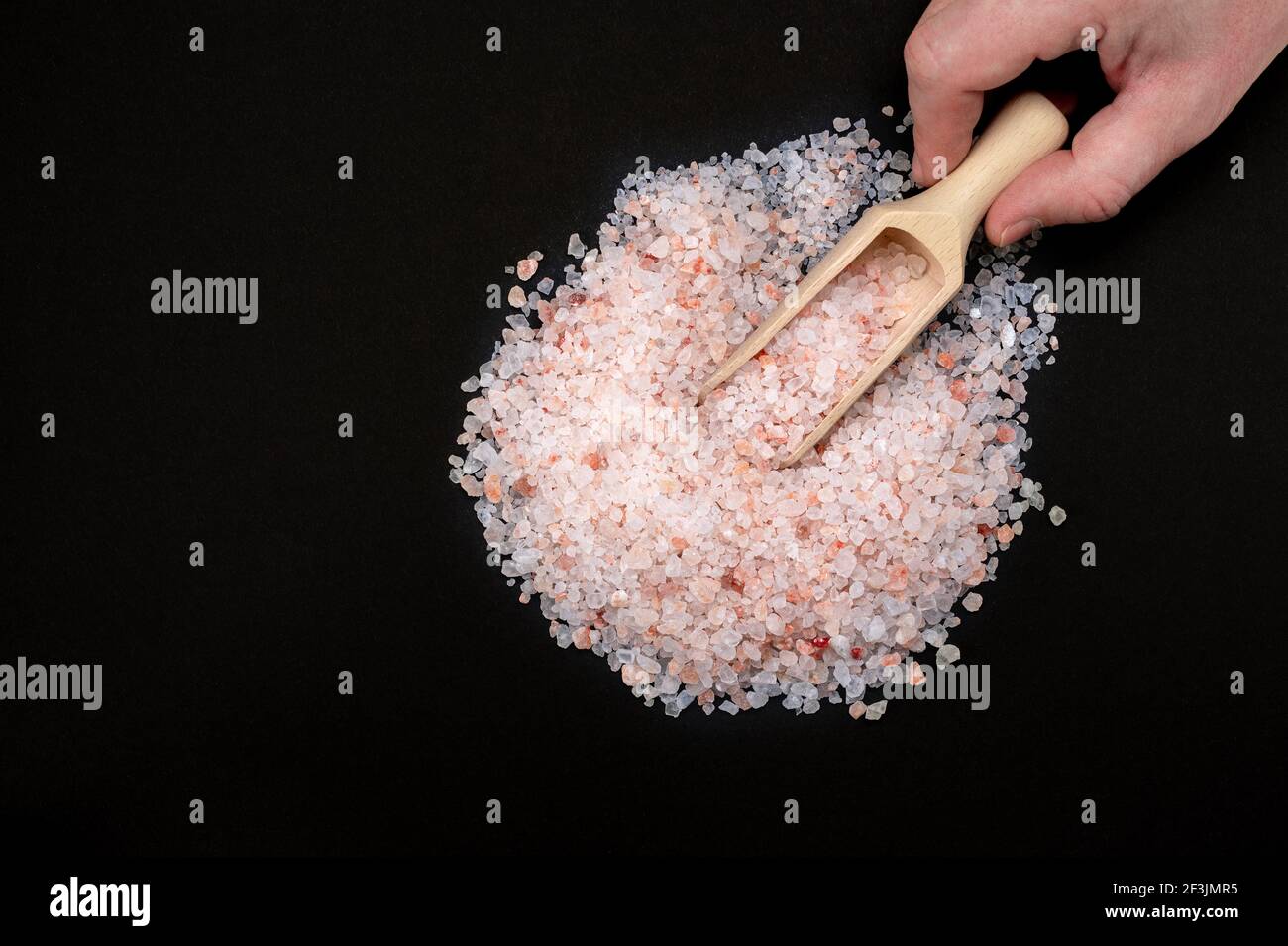 Rosa himalaya-Salz. Himalayan Pink Rock Salt in Holzlöffel auf schwarzem Hintergrund. Draufsicht, Kopierraum. Hand halten Holzlöffel mit Pink himalayan sa Stockfoto